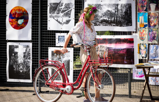 Kobieta oparta o czerwony rower ogląda prace graficzne