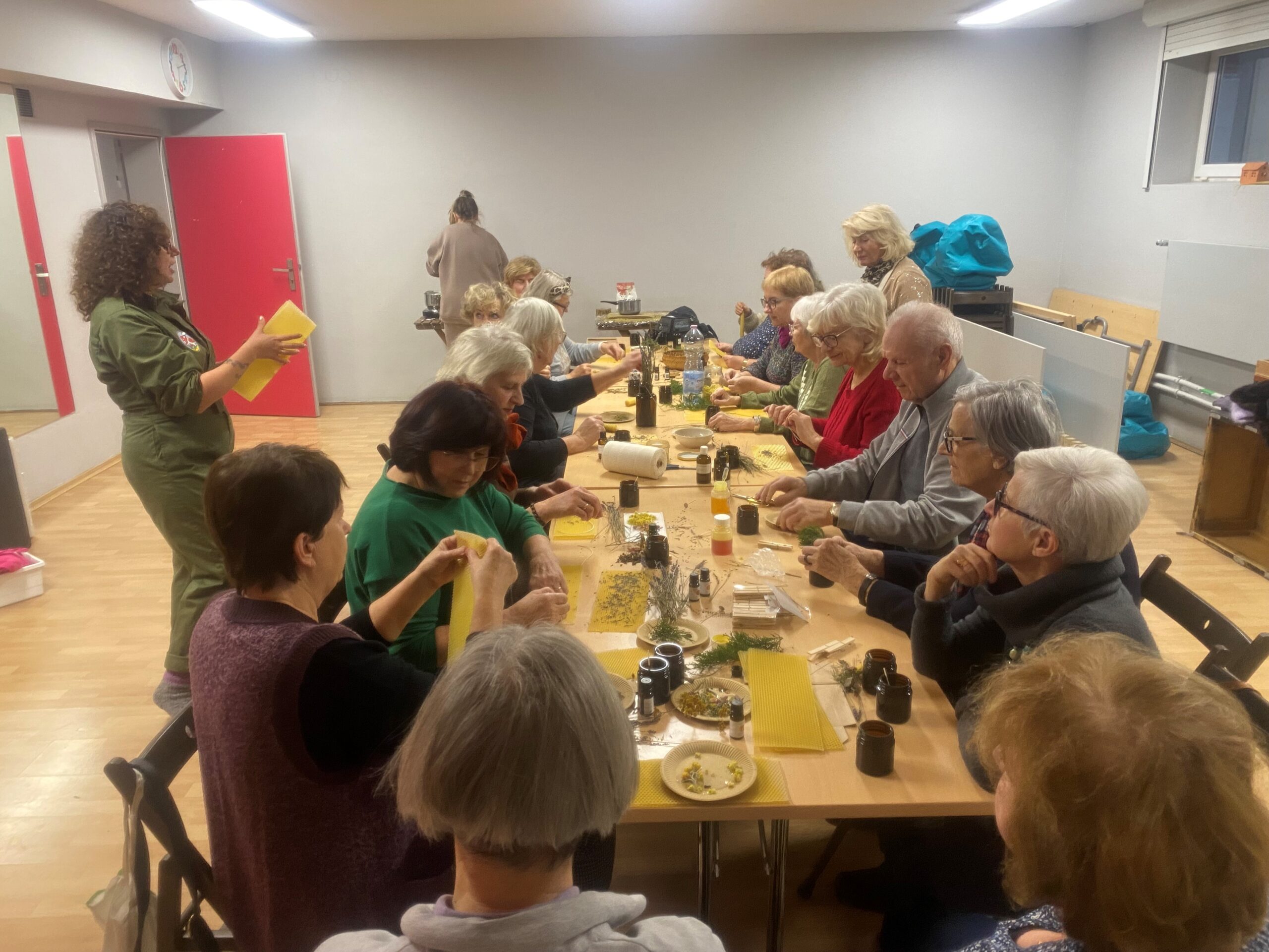 Grupa seniorów siedzi przy stole zasawionym produktami do robienia świec z wosku