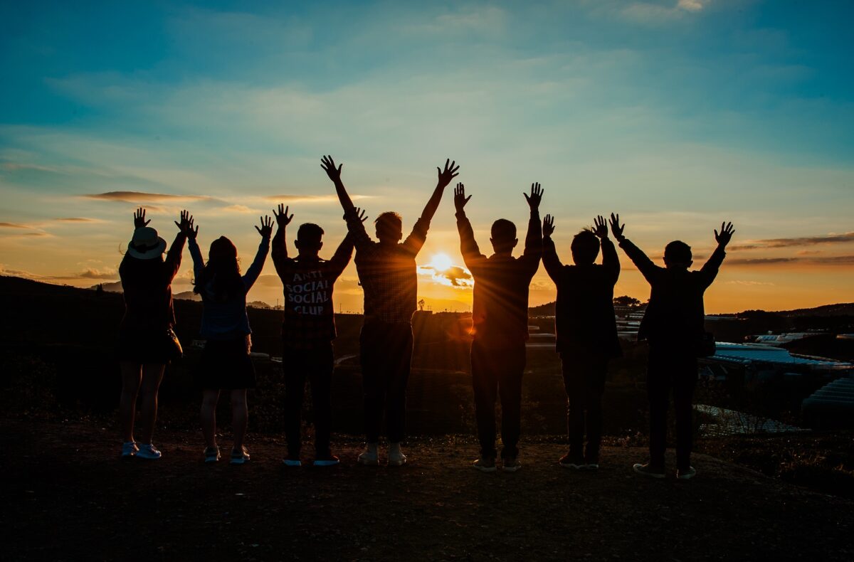 Grupa młodzieży z rękami do góry na tle zachodzącego słońca