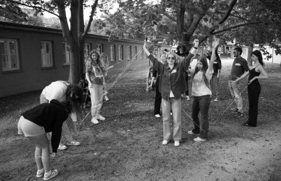 Grupa młodych ludzi na trawniku z drzewami, robi instalację ze sznurka