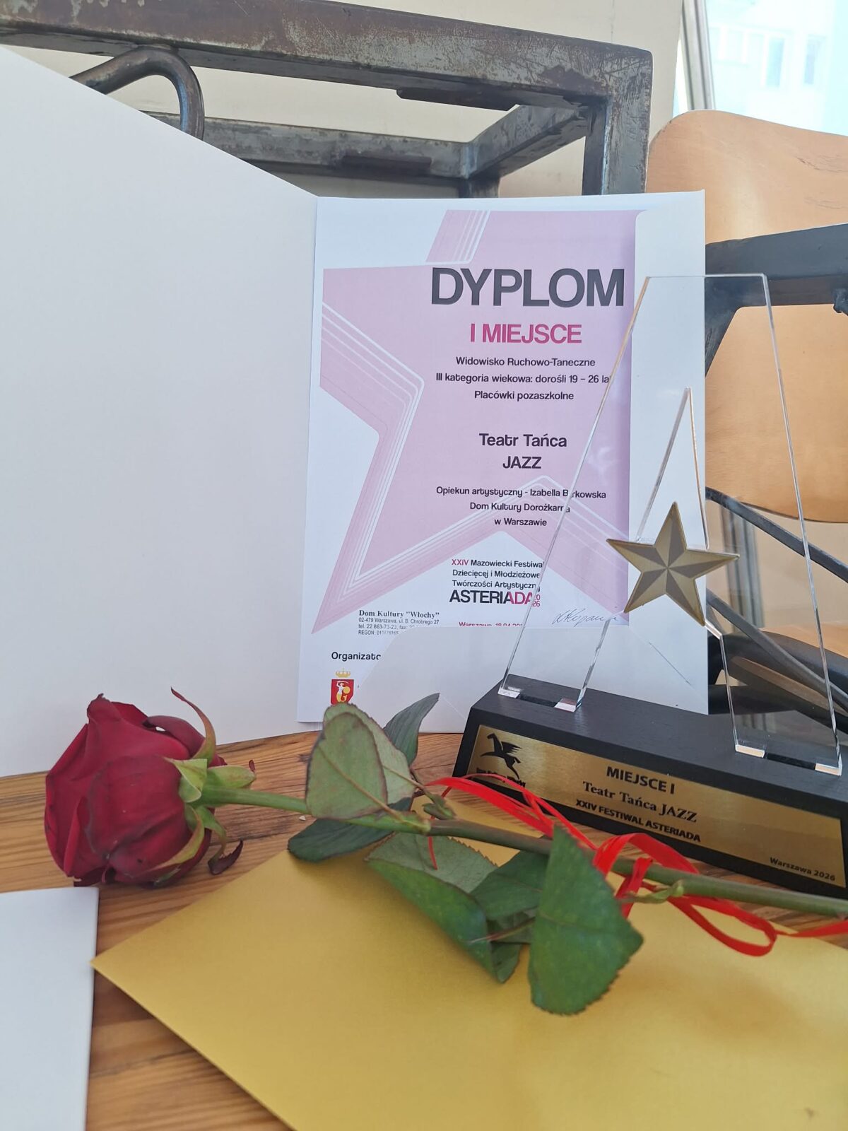 Zdjęcie amatorskie. Widoczny dyplom za zajęcie pierwszego miejsca i kwiat - róża.