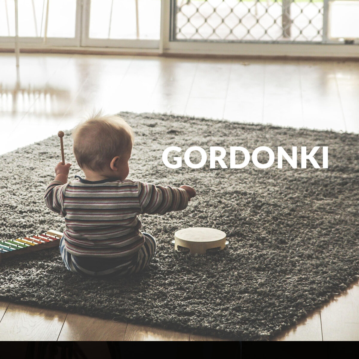 Zdjęcie siedzącego niemowlęcia z bębenkiem. Napis "Gordonki"