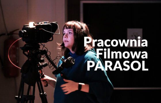 Zdjęcie kobiety wpatrzonej w kamerę. Rejestruje wydarzenie. Napis "Pracownia Filmowa PARASOL"